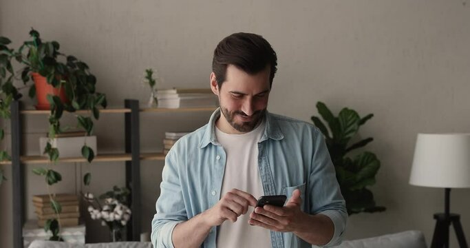 Businessman with smartphone standing indoor. Millennial guy smiling use cellphone, share messages, communicates remotely, browse internet feel satisfied. Modern tech usage for business or fun concept