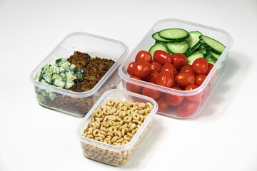 closeup of plastic containers filled with cereal, salad, tomatoes, and more, on a white surface
