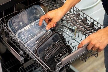 closeup of a woman putting plastic containers in a dishwasher, in a kitchen indoors