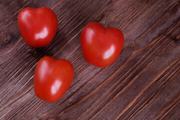 Obraz na płótnie Canvas Three red heart-shaped tomatoes lie on a wooden surface. Top view. Vegetarian food as a concept