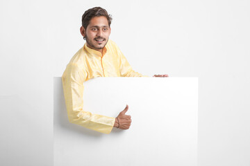 Indian man holding white board, promoting offers on festival season while wearing traditional cloths, standing over white background.