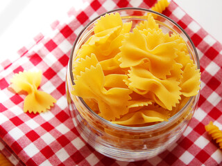 raw farfalle pasta in a bowl, italian pasta - farfalle in a glass bowl on a white background. Various types of Italian durum wheat pasta for Mediterranean cuisine. Top view, place for text. Banner.