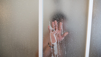 naked girl in shower washing her hair and sliding her hand with foam on the glass