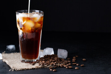 cold iced coffee brew with milk or cream on a black background coffee beans, summer drink