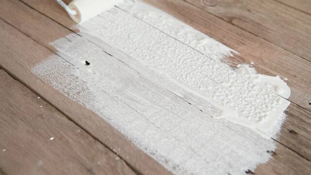 A house painter paints old boards with white paint.