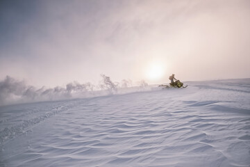 Snowmobile female rider riding on beautiful mountain slope