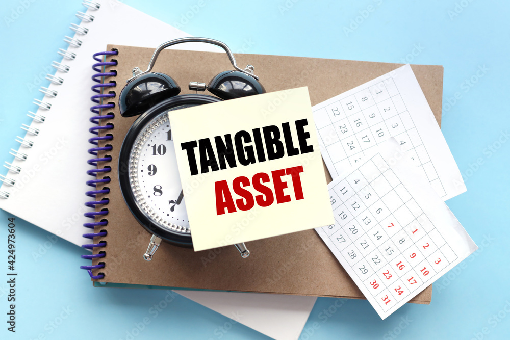 Poster tangible asset. text on the sticker attached to the alarm clock. alarm clock on notepad on blue back
