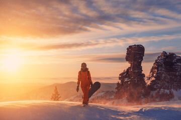 Silhouette of snowboarder female walking with snowboard during sunset