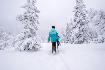 Fototapeta na wymiar Snowboarder female walking through the forest carrying snowboard. Powder Day. Walking throw deep snow, snowboarder on winter holiday