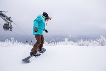 Snowboarder female riding on winter snow cowered slop on snowboard. Gondola lift in the ski resort,...