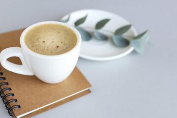 Coffee white cup and blank notepad and plant on gray solid background. Side view with copy space. close-up. business concept