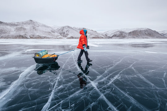 Female tourist walking with  sled dragging on the frozen ice of Lake Baikal. Winter trekking