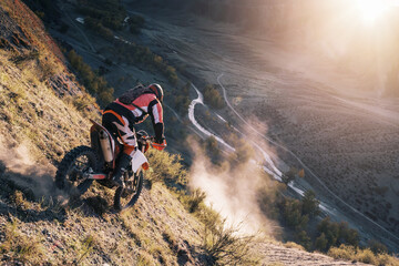 Extreme Rider climbing sand mountain top on off-road cross enduro motorcycle. Beautiful mountains landscape down on background, colourful autumn forest and river in sunshine © Annatamila