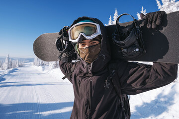 Portrait of a snowboarder standing with  board on the snow in winter ski resort