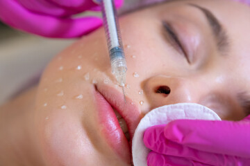 Cosmetologist applying a woman a cosmetic medical gel in a face from a syringe. Woman in a spa salon on cosmetic procedures for facial care.  Beautician makes skin care procedure on a  face. .