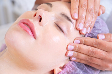 Woman in a spa salon getting face massage for facial care. Beautician makes a massage of the  face with a moisturizing mask on a face.  Beauty treatment concept.