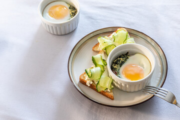 Shirred eggs (Oeuf cocotte) or baked eggs. healthy breakfast with eggs and spinach and toast with cucumber