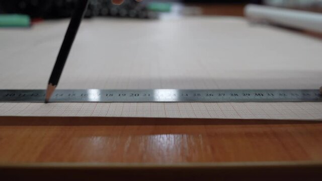 close-up of a sheet of graph paper, a female hand applies a ruler and draws a line with a pencil. concept designer works.