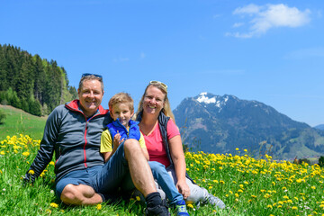 Gutgelaunte Familie sitzt auf einer Wiese im Allgäu und genießt die frühlingshafte Natur