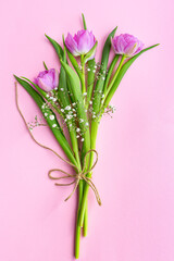 Romantic delicate bouquet of pink tulips and gypsophila tied with a jute rope on a pink background. Greeting card for mother's day, March 8 or wedding. Floristics, flower shop. Eco-friendly packaging.