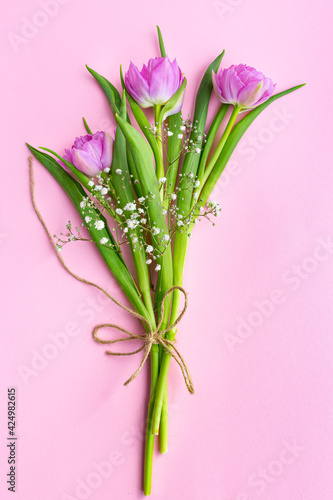 Romantic delicate bouquet of pink tulips and gypsophila tied with a jute rope on a pink background. Greeting card for mother's day, March 8 or wedding. Floristics, flower shop. Eco-friendly packaging.