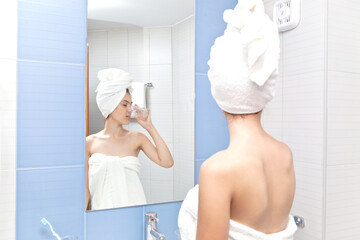 Beautiful young girl in a bath white towel in the bathroom drinks water from a glass