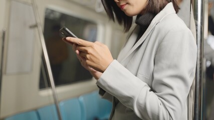 Asian female businessmen Reply to chat messages And use the phone on the skytrain or subway their way to working transportation. She discussion business on his phone while traveling to meet a partner.
