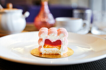A pink mousse cake with raspberry jelly and banana filling on a white plate in a restaurant,...