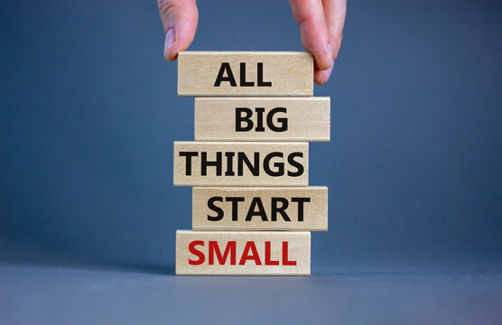 Business concept growth success process. Wood blocks on grey background, copy space. Businessman hand. Words 'all big things start small'. Conceptual image of motivation.