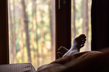 Man's feet on the bed, a view of the pine forest of Thailand.