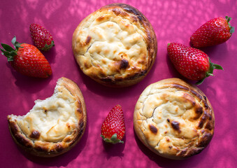 Freshly baked cream-cheese buns and strawberries on pink background. Appetizing pastries with cottage. 
