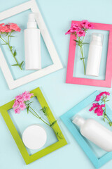 Cosmetics for skin care face, body, hands. White blank cosmetic bottle, tube, jar, flowers in bright frames on blue background. Creative Cosmetic Beauty Concept. Mockup Top view