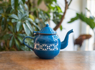 Mid-century modern blue enameled kettle on a wooden table with plants in the background