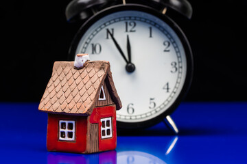Model of cardboard house with alarm clock, real estate, cost of housing or buying a new home...