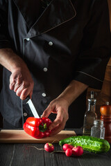 Close-up of a chef hands cutting peppers on cutting board. Professional preparation of salad in the kitchen in a restaurant or cafe