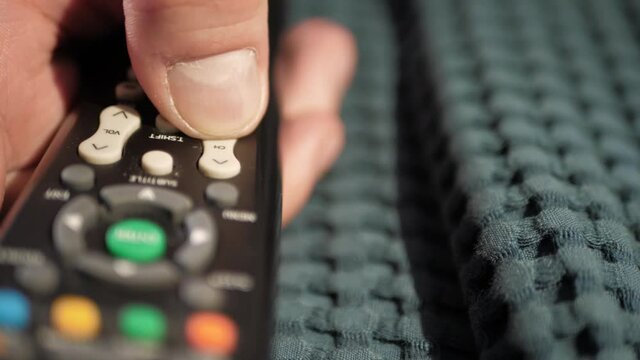 Man hand presses buttons on remote control switching TV channels. Close-up