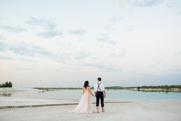 young couple a guy in black breeches and a girl in a pink dress are walking along the white sand