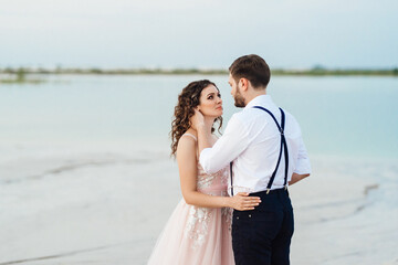 young couple a guy in black breeches and a girl in a pink dress are walking along the white sand