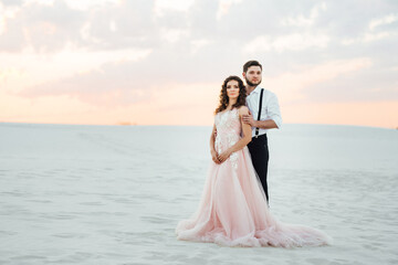 Fototapeta na wymiar young couple a guy in black breeches and a girl in a pink dress are walking along the white sand