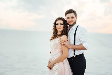 Obraz premium young couple a guy in black breeches and a girl in a pink dress are walking along the white sand