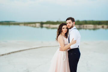 young couple a guy in black breeches and a girl in a pink dress are walking along the white sand