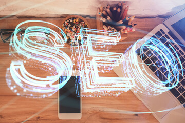 Double exposure of SEO hologram drawing over desktop. Top view. Search optimization concept.