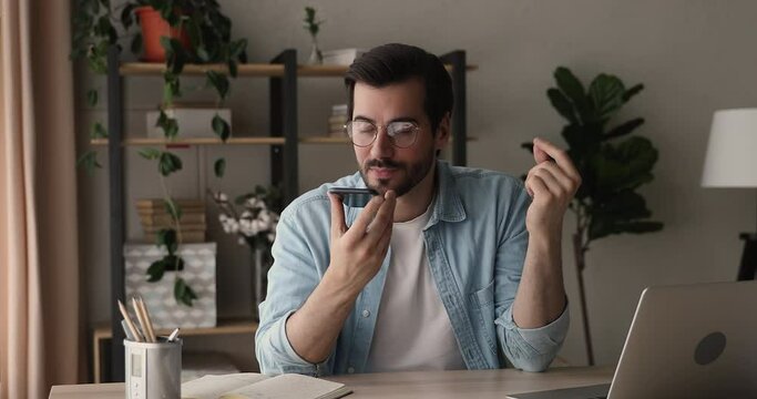 Businessman sit at desk hold smart phone calling use speaker phone chat to client provide helpful information remotely, makes short talk. Modern tech loudspeaker usage, distant conversation concept