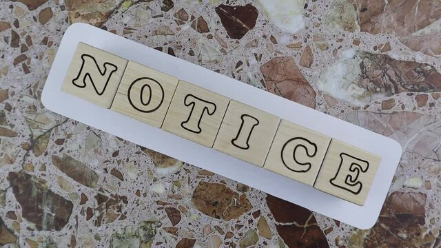 Notice - design template with alphabet letters on wooden cubes arranged over a white sign centered on a marbled stone background with copyspace. Rotating table