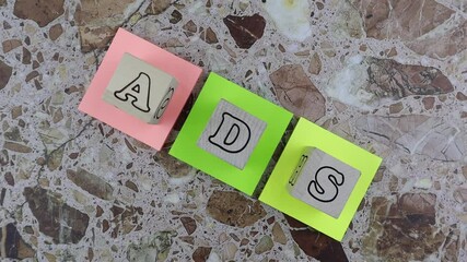 ADS concept with wooden cubes with alphabet letters arranged on three brightly colored memo pads over a marbled stone background. Rotation - Powered by Adobe