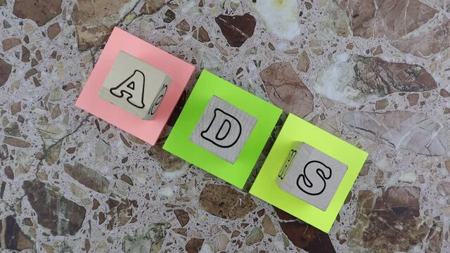 ADS concept with wooden cubes with alphabet letters arranged on three brightly colored memo pads over a marbled stone background. Rotation