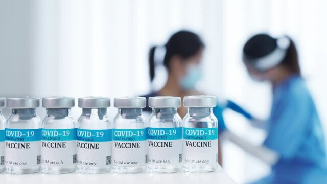 Many vaccine vial bottle in background of young female asian doctor, scrub nurse hold syringe injection to asia volunteer mature adult woman in healthcare medical protect prevent covid19 coronavirus.