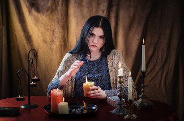 young witch conjures with burning candles on  dark background