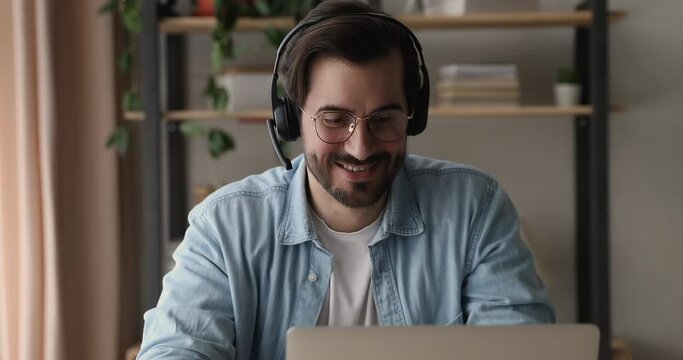 Millennial confident businessman sit at workplace look at laptop listen to client through headset talk to customer using remote web chat online video conference application. Video call event concept