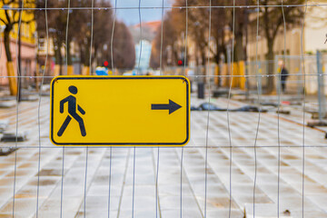 Building fence directing pedestrians. Yellow sign with the direction of pedestrian traffic